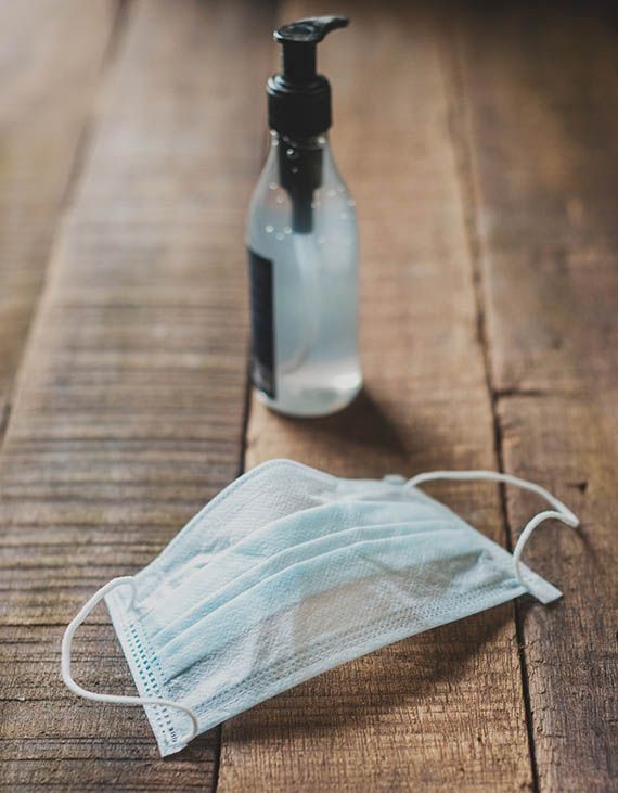 Surgical face mask and liquid dispensing bottle sitting on wooden table