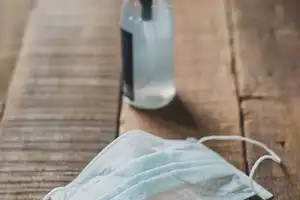 Surgical face mask and liquid dispensing bottle sitting on wooden table