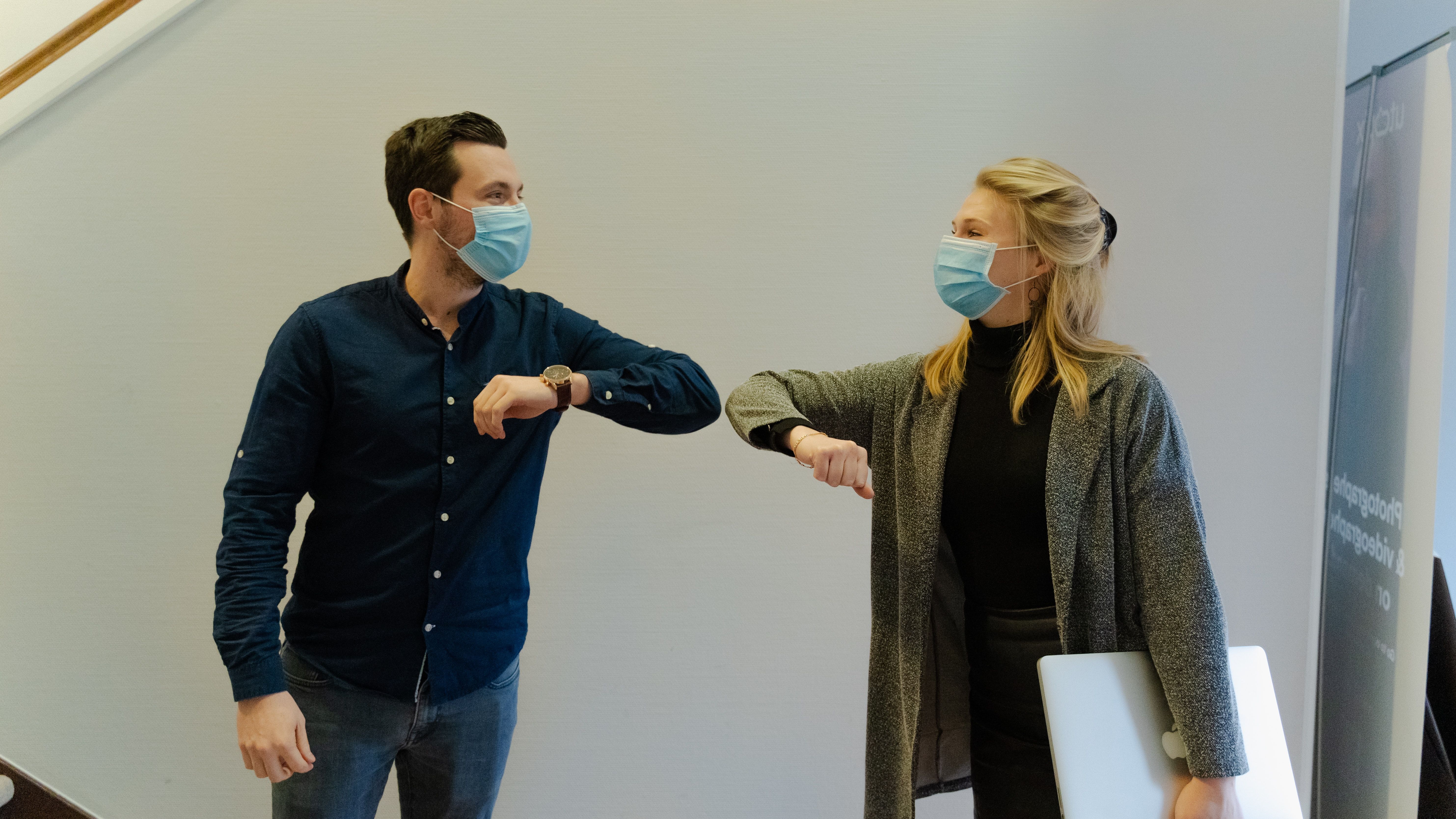 Two people wearing medical face masks and touching elbows as a greeting