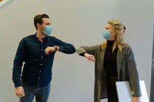 Two people wearing medical face masks and touching elbows as a greeting